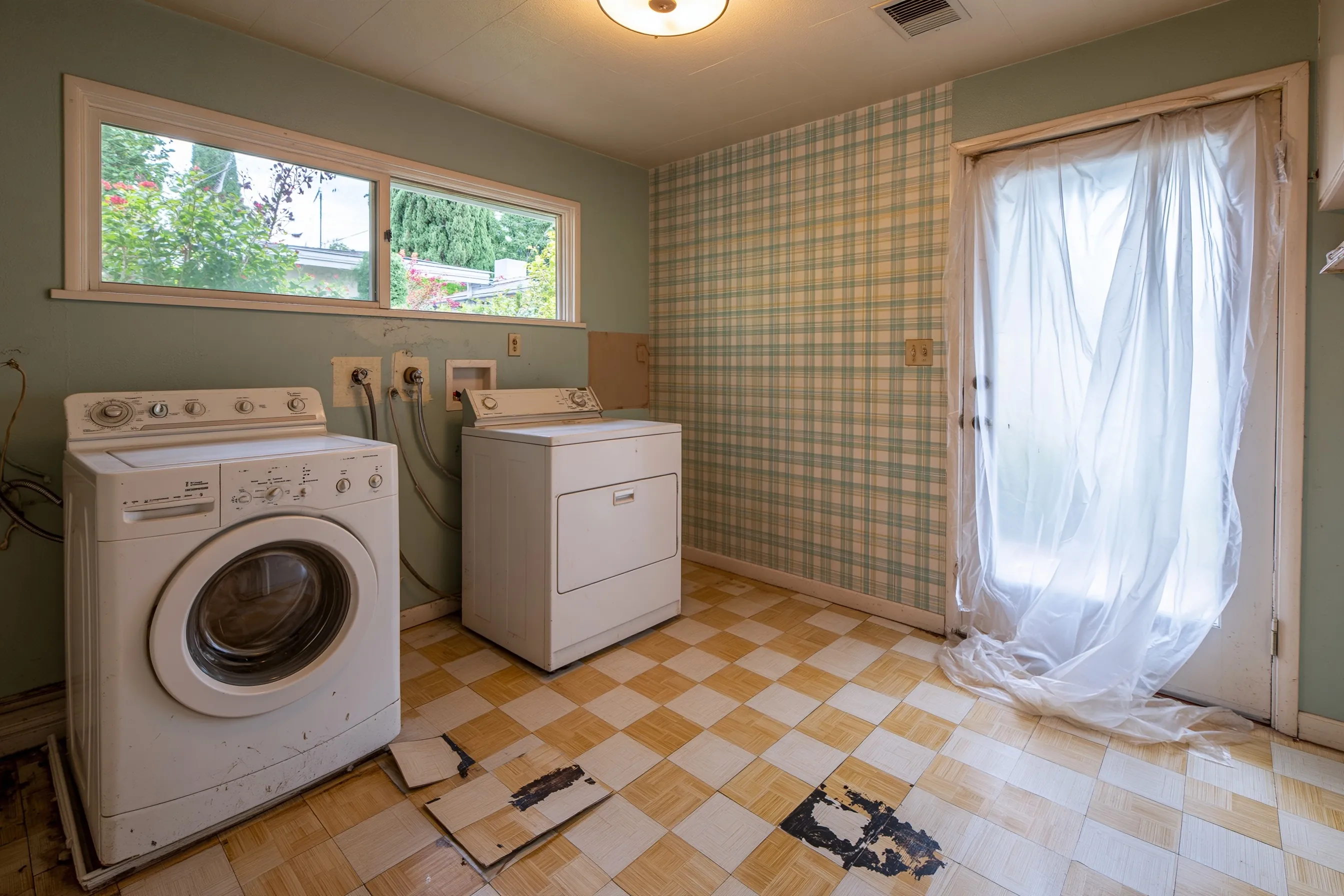 A 1960s laundry room with the washer and dryer moved out and 9-inch tiles lifted to show black adhesive